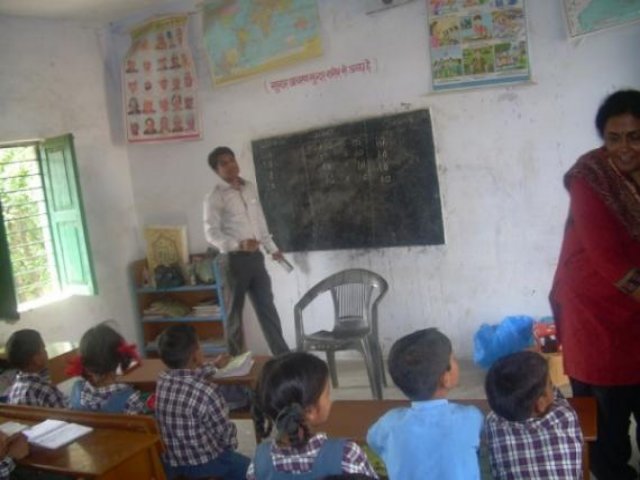 A lesson in progress, the children seated on the floor before the blackboard.
