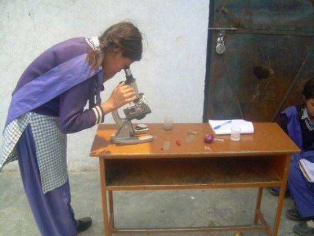 A pupil looking into a microscope at a table by the window.