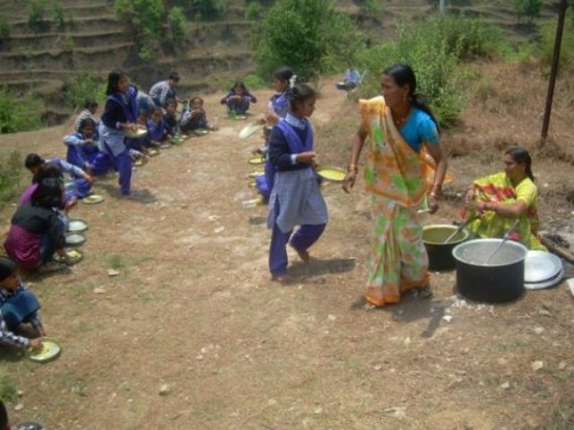 Children being served a meal from cooking pots on the hillside.