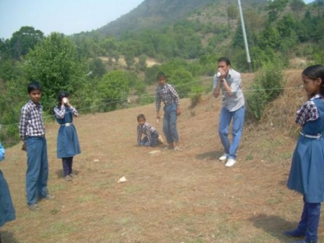 Children on the grassy hillside using hand-held instruments.