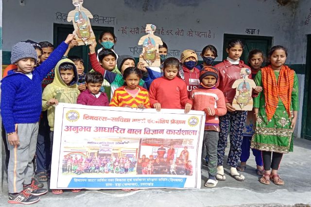 Children outside, one of them holding up a poster, the programme banner behind.