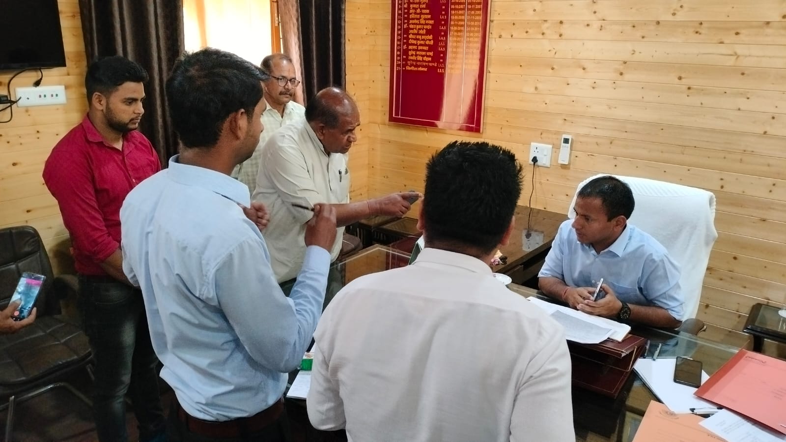 Men gathered around the desks in a wood-panelled office.