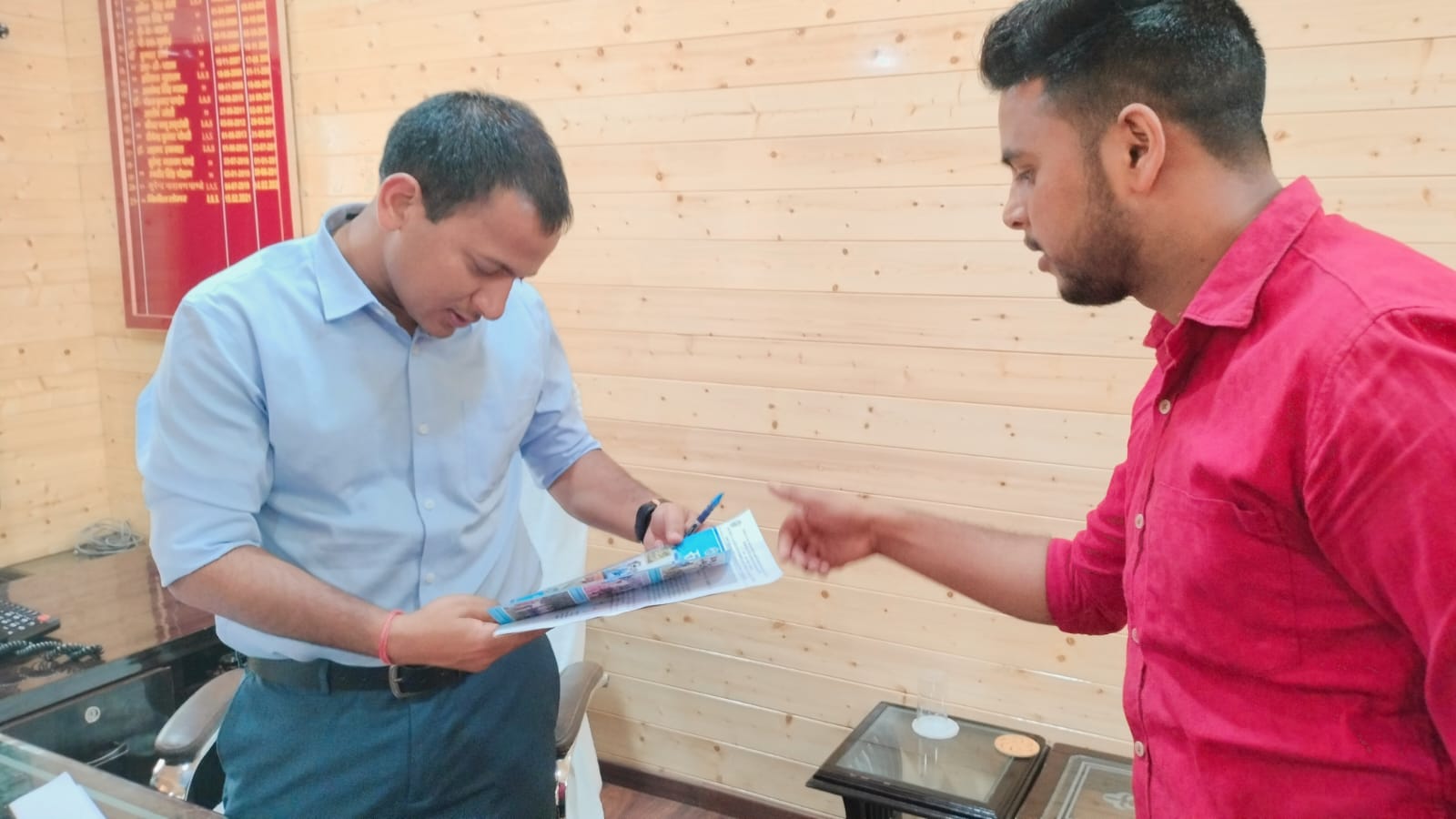 Two men exchanging documents across the desk.