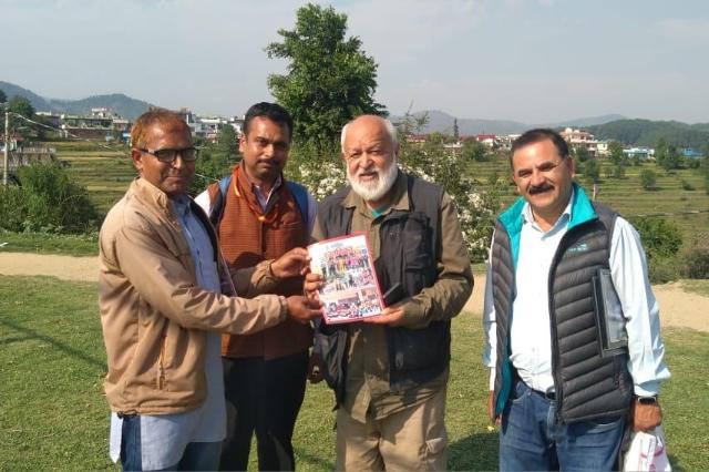 A book being handed over at the Kitab Kauthig book fair, with the hills behind.