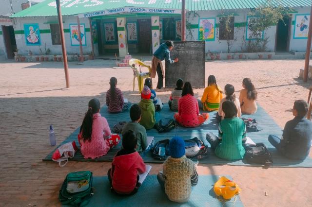 Children seated on mats in the yard for a Navodaya entrance preparation class.