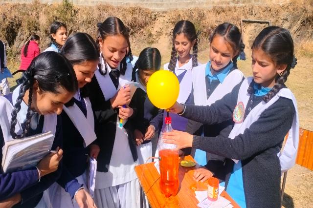 Girls carrying out a balloon-and-bottle experiment at the UCOST science fair.
