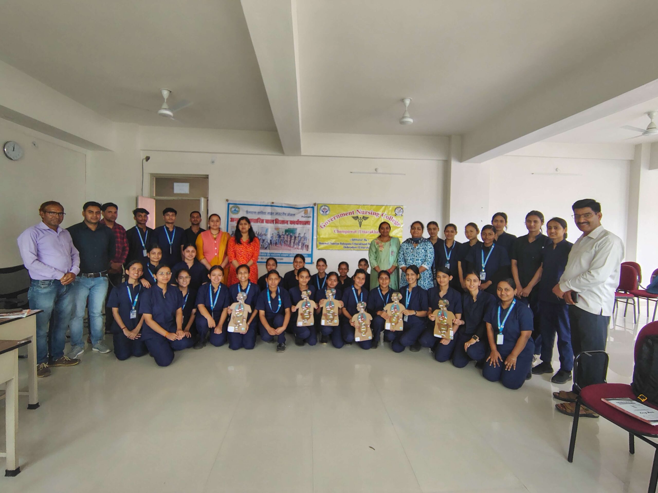 A large group of students holding certificates in a hall at a nursing college session.
