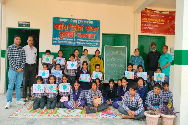 Children holding hand-drawn Earth Day posters in the classroom, their teachers behind them.
