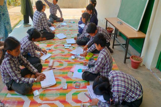 Children sitting on mats on the floor, making Earth Day posters.