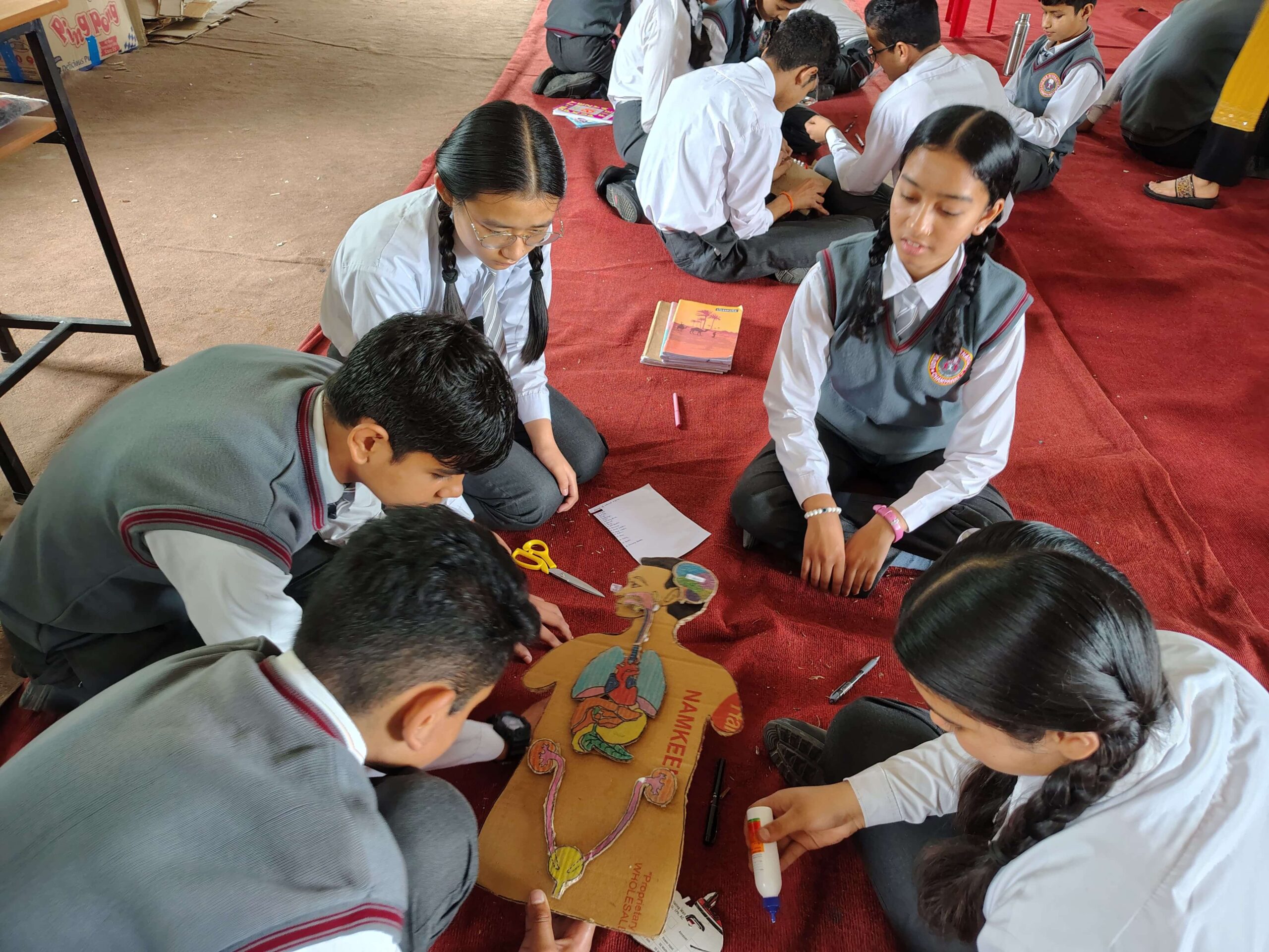 Students building a model of the human body at a table covered with red cloth.