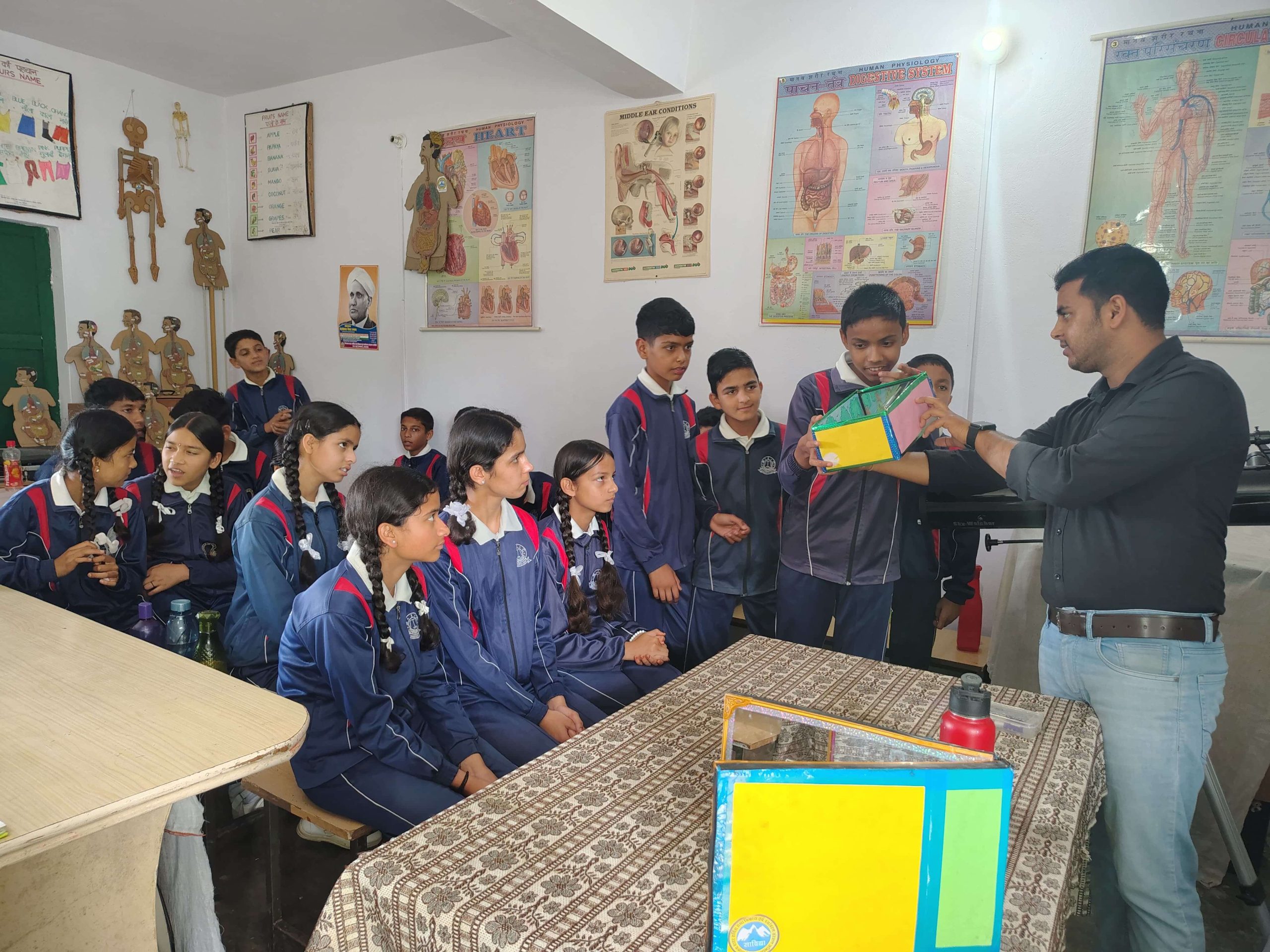 A volunteer holding up coloured card to a group of visiting students, an anatomical model on the wall behind.