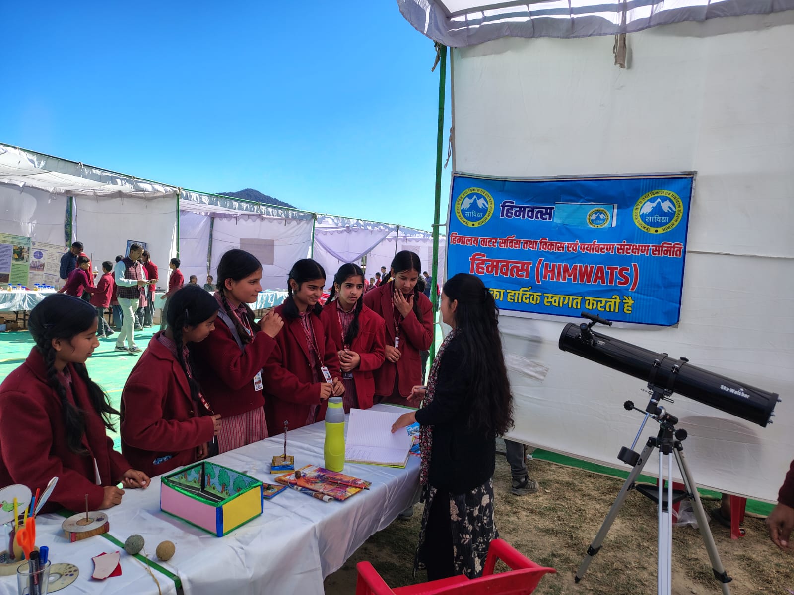 A telescope set up on its tripod beside the exhibit tables, under the marquee.
