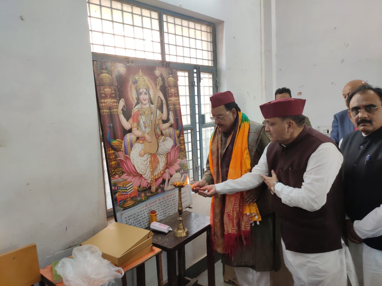 Guests in Kumaoni caps at a lamp-lighting ceremony beside a garlanded portrait.