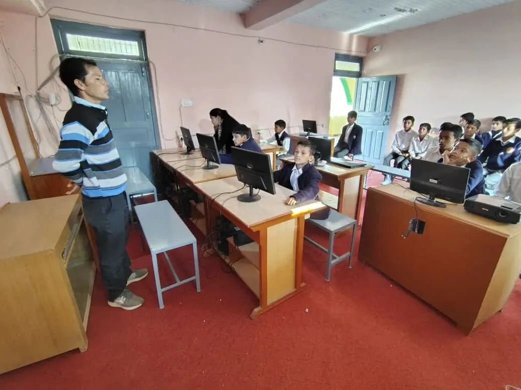 A class in the HIMWATS Digital Learning Center at VVMIC — a teacher standing at the front, pupils at the terminals along two rows of desks, and more seated waiting their turn.