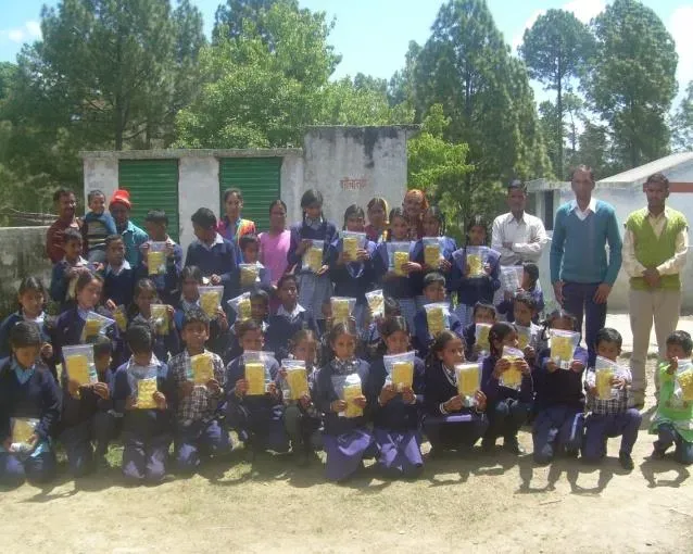 Schoolchildren standing in rows outside, each holding up a packet of health supplements.
