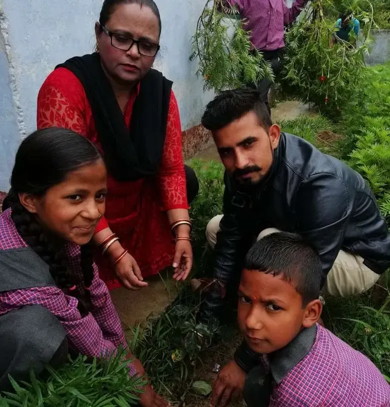 A sapling being planted on a hillside, watched by two children.